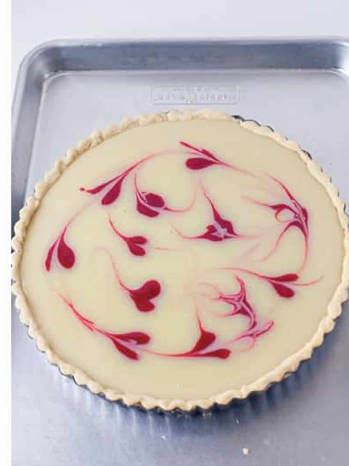 Finished white chocolate raspberry tart with swirled raspberry hearts on top.