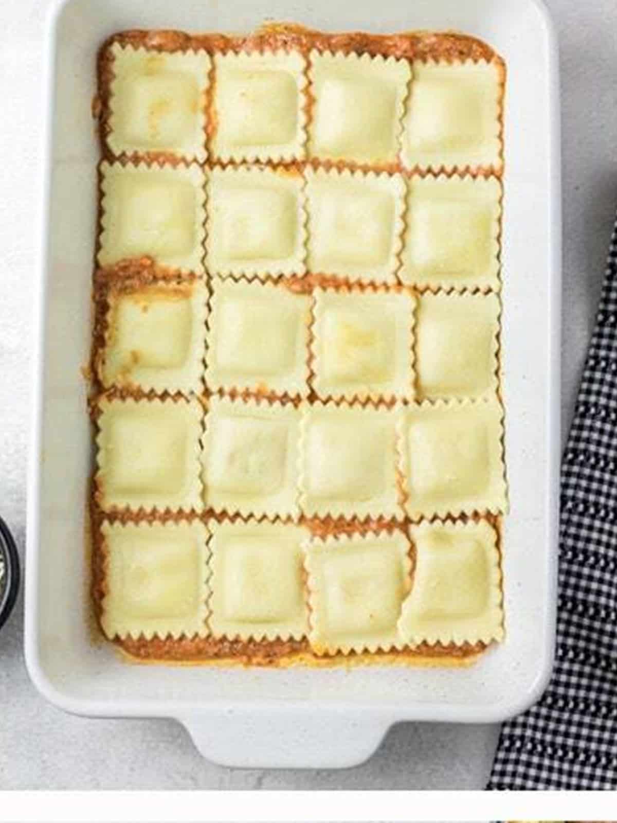 A layer of cheese ravioli arranged over sauce in a white baking dish.