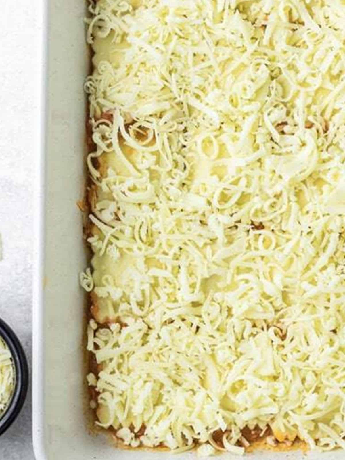 Shredded mozzarella cheese spread over the top of layered ravioli lasagna.