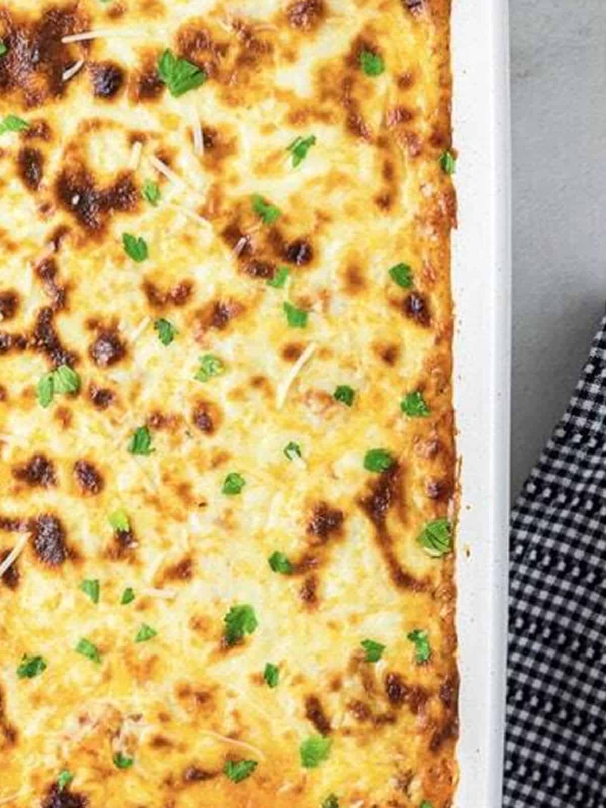 Golden bubbly baked ravioli lasagna in a white baking dish.
