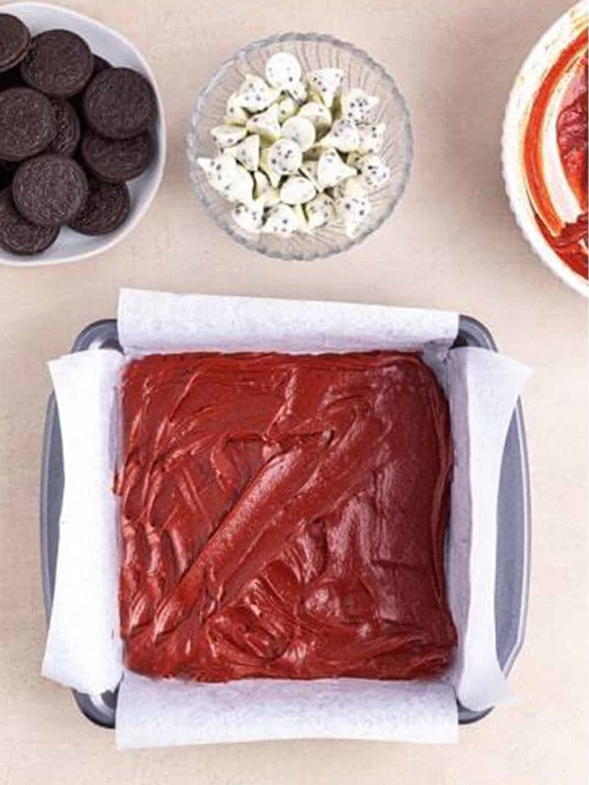 Half the red velvet brownie batter spread in a parchment-lined pan.