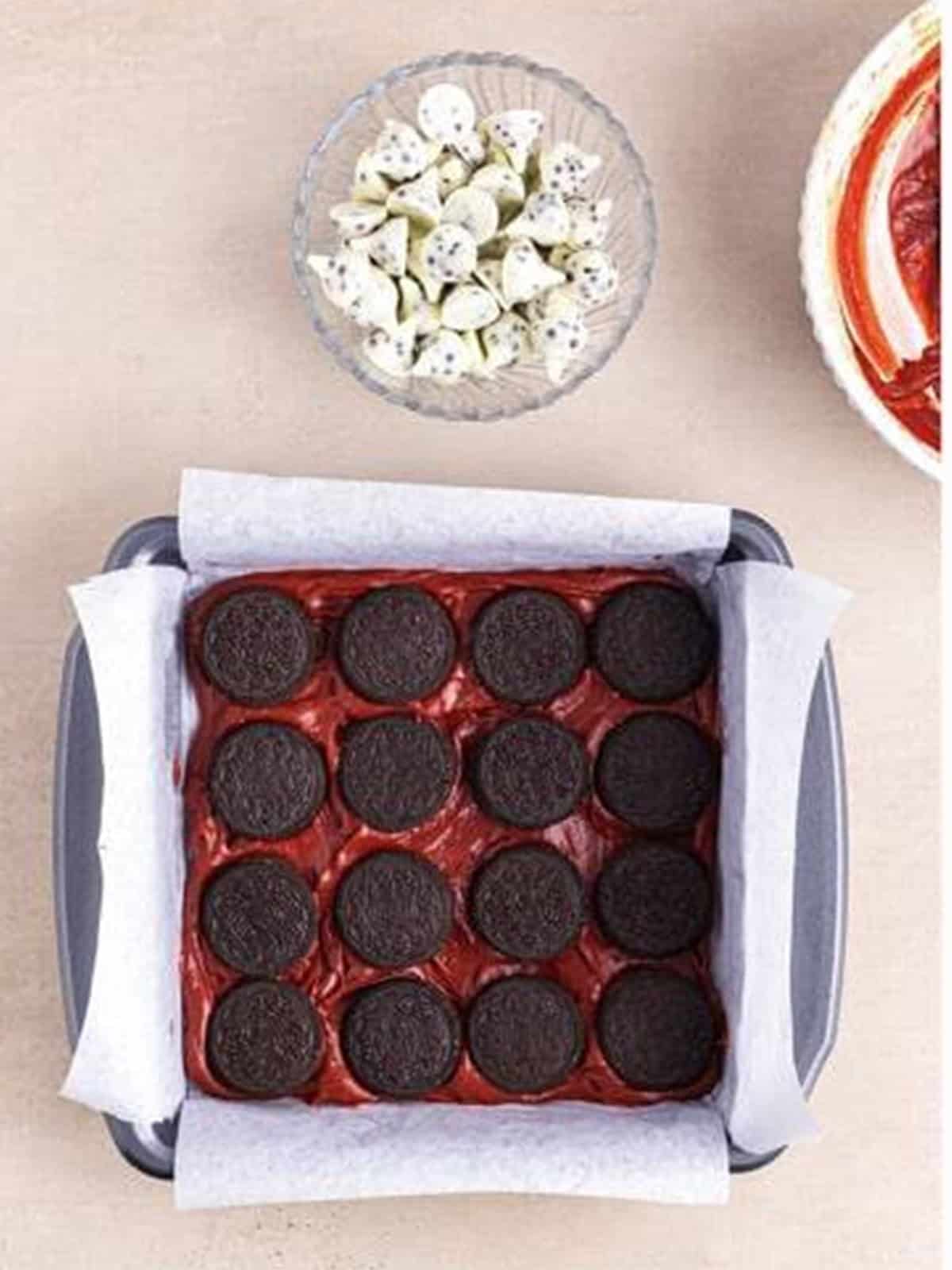 A layer of Oreos arranged over the red velvet batter in the pan.