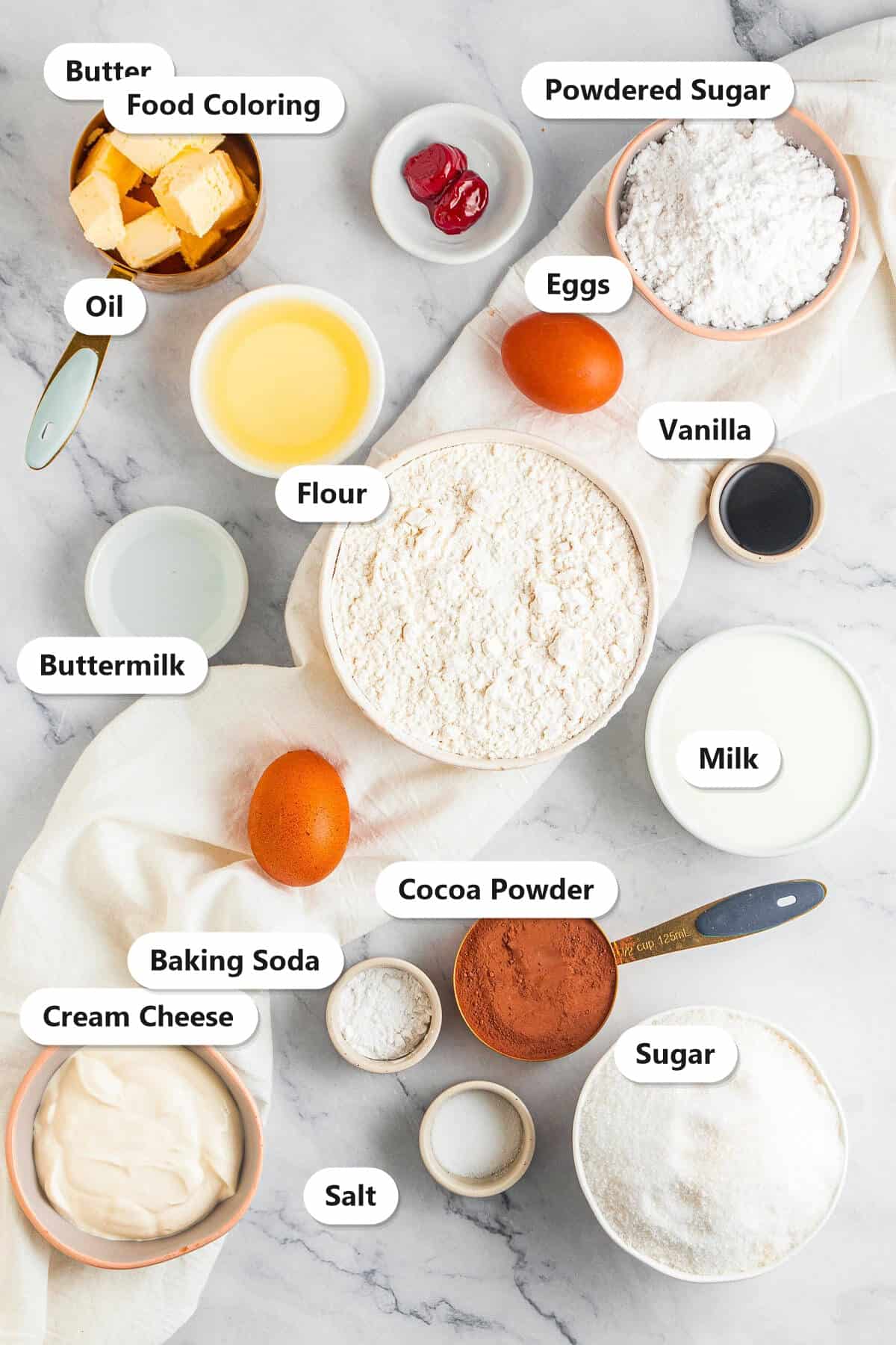 Labeled ingredients for red velvet bundt cake including flour, cocoa, sugar, buttermilk, oil, eggs, red food coloring, and cream cheese.