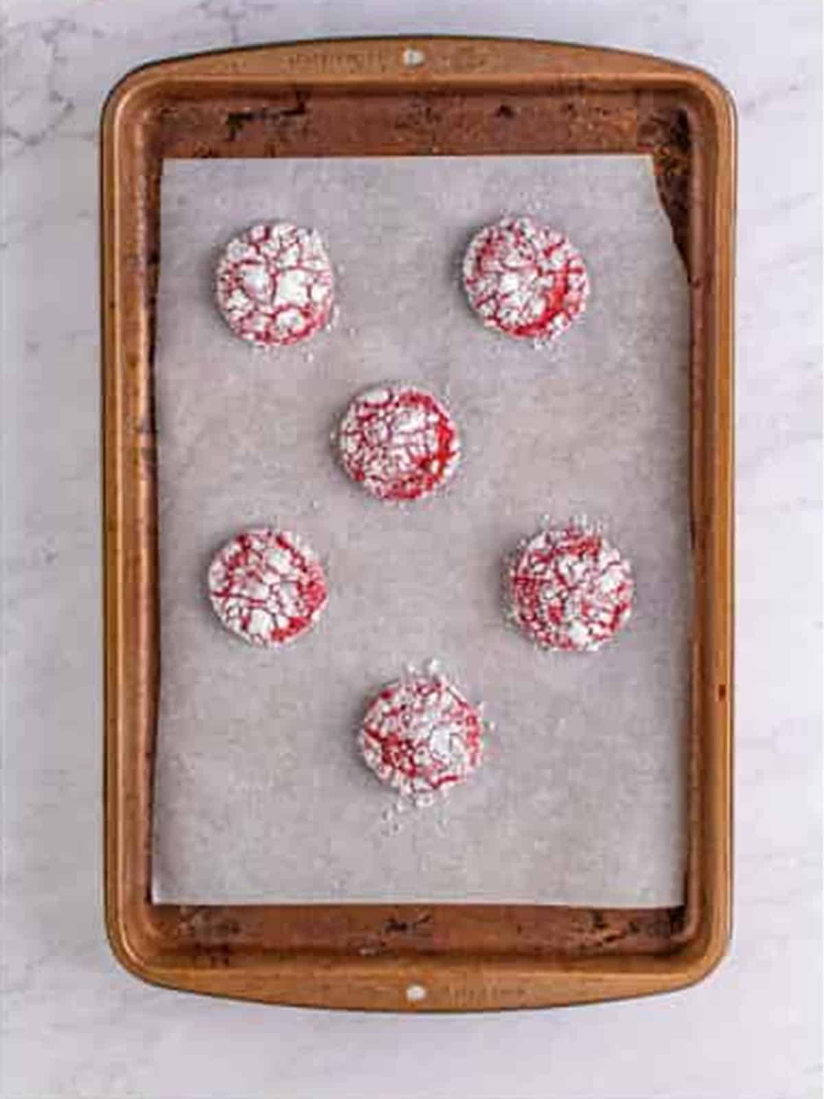 Baked crackled red velvet cookies on a parchment-lined sheet tray.