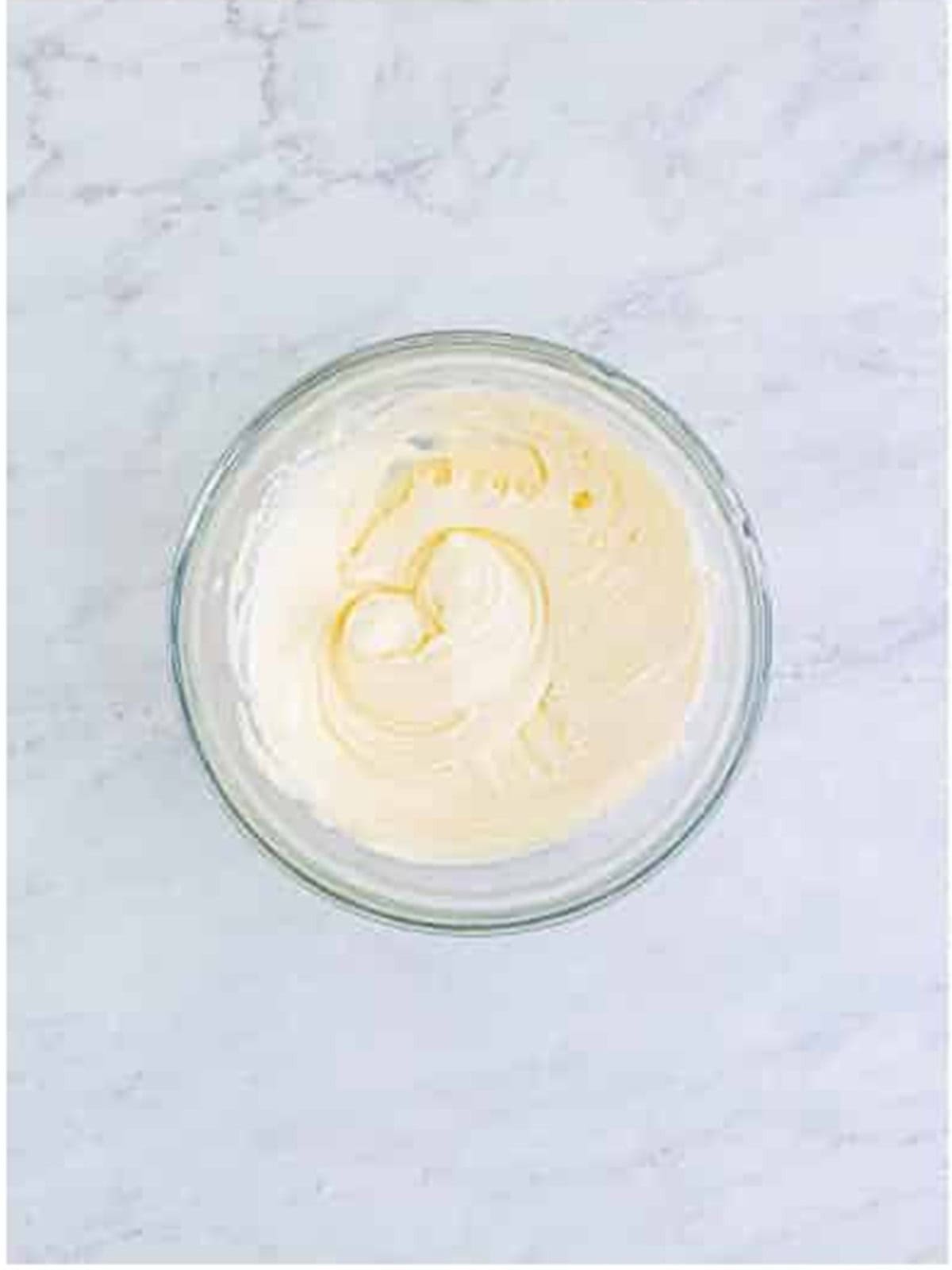 Cream cheese frosting whipped smooth in a glass bowl.