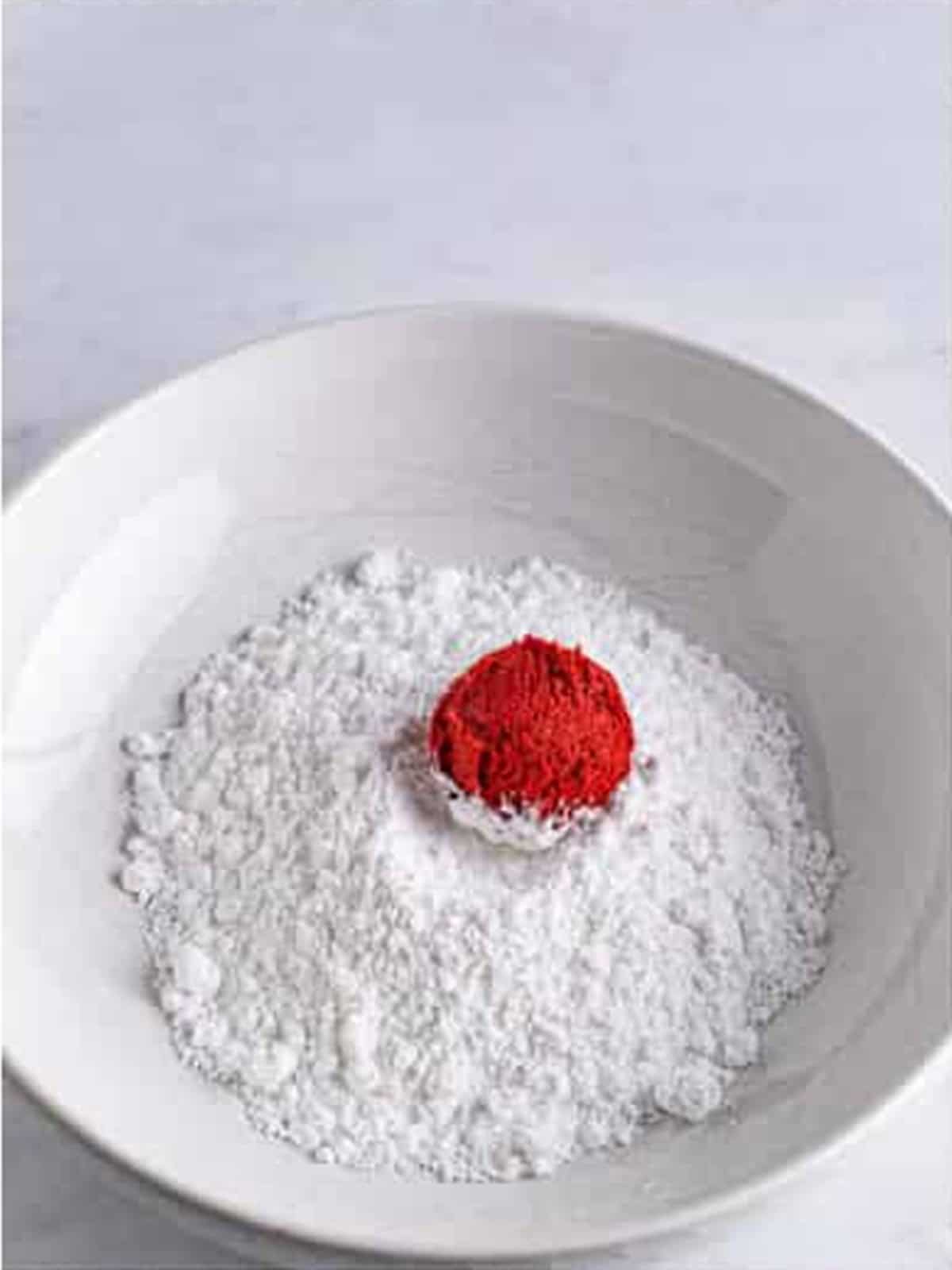 Red velvet cookie dough ball rolled in powdered sugar.