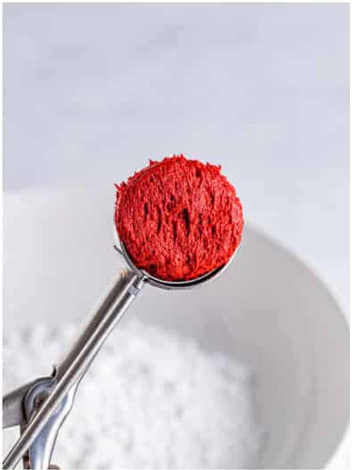 Scooping a ball of red velvet cookie dough over powdered sugar.