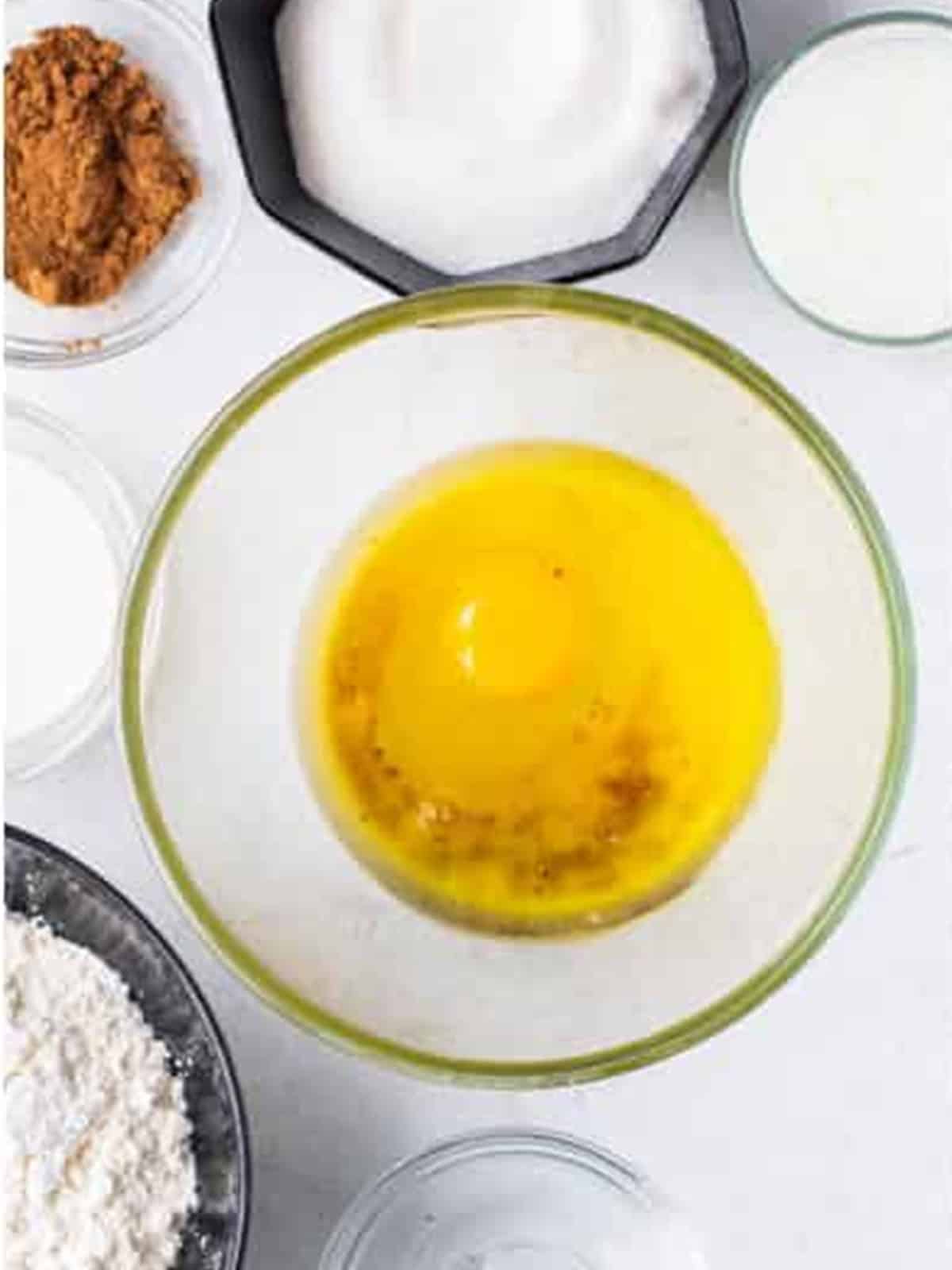 Vegetable oil, butter, egg, vanilla, and sugar mixed together in a bowl for red velvet cupcake batter.