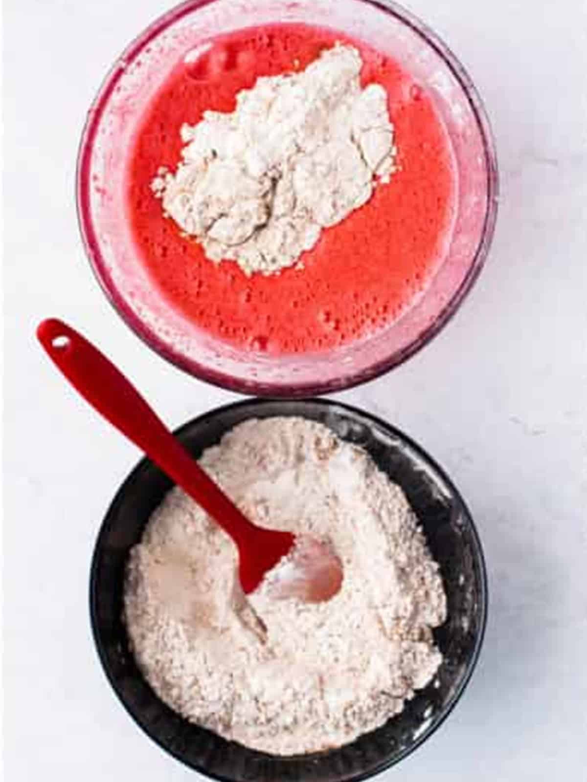 Red velvet cupcake batter spooned into a cupcake pan lined with white liners.