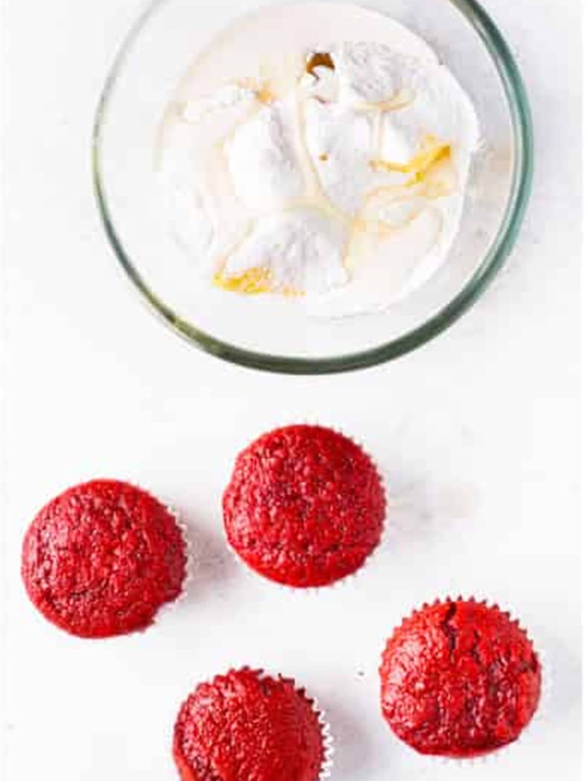 Red velvet cupcakes topped with swirls of fluffy cream cheese frosting and red sprinkles.