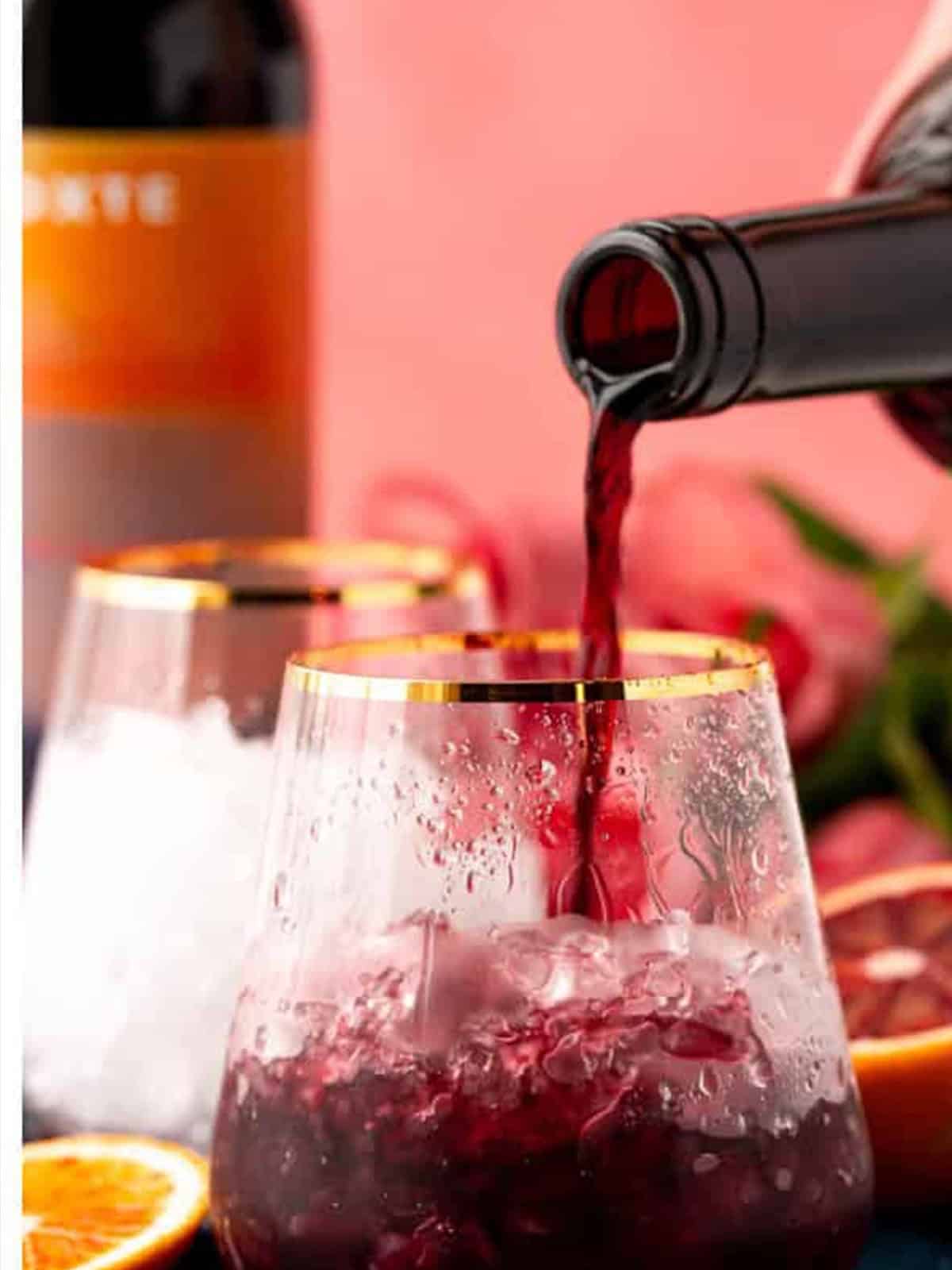 Red wine being poured into a glass filled with ice.