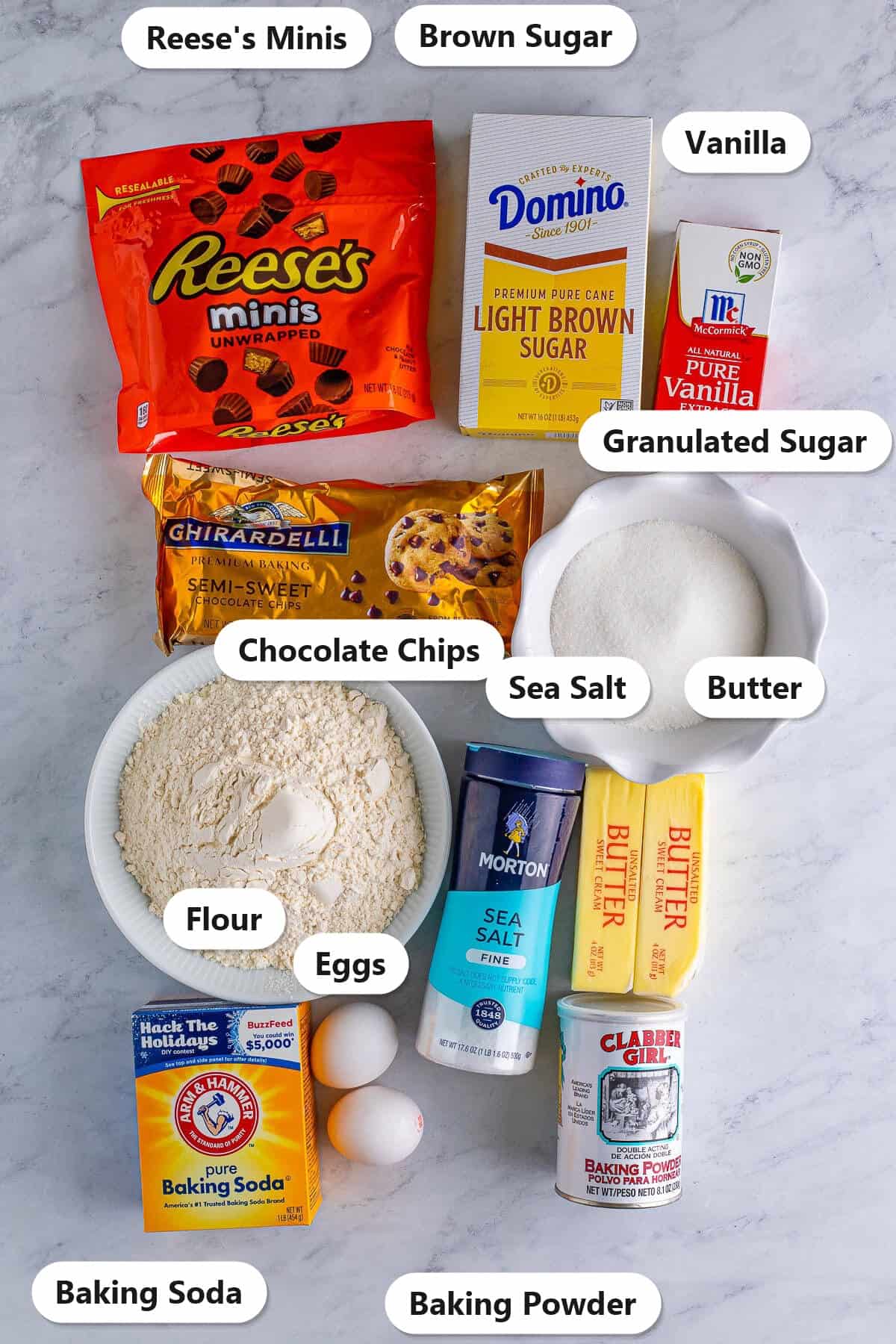 Labeled ingredients needed to make Reese's Peanut Butter Cup Cookies including mini Reese's, chocolate chips, flour, sugars, butter, eggs, and vanilla.