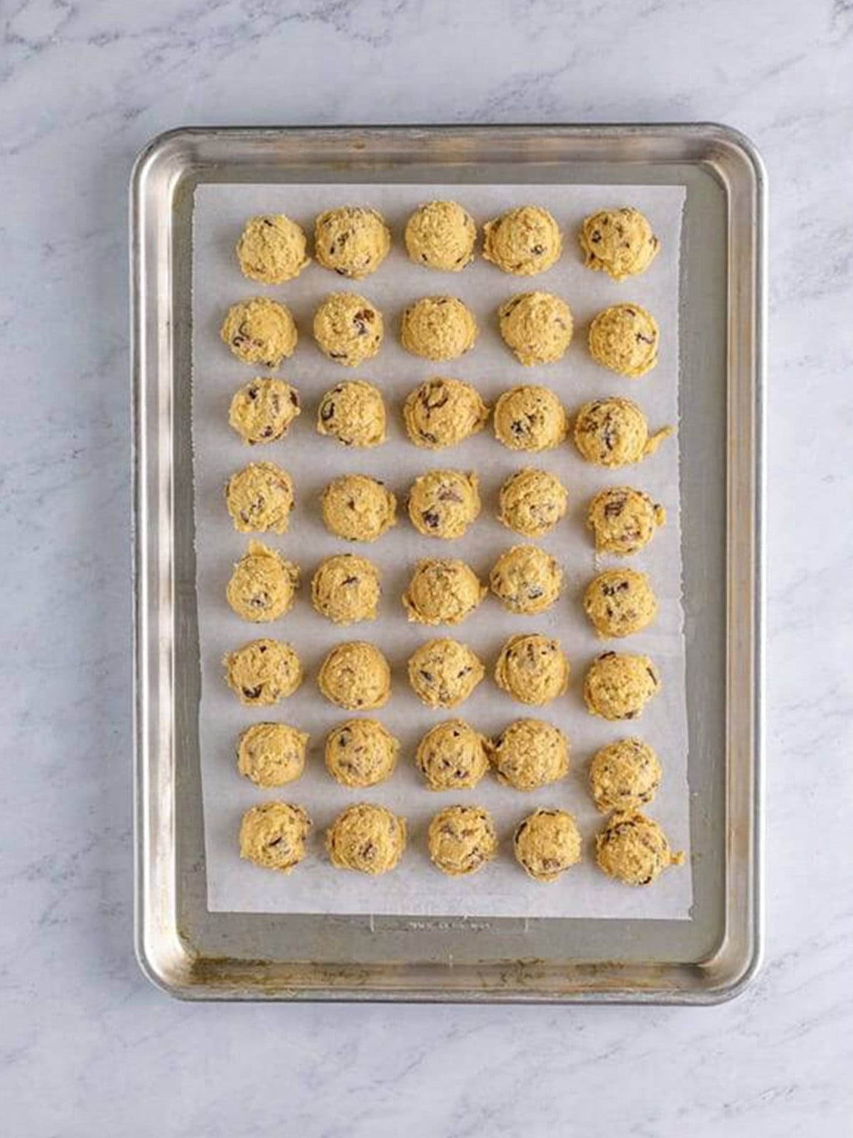 Cookie dough scooped into portions packed closely on a parchment lined tray for chilling.