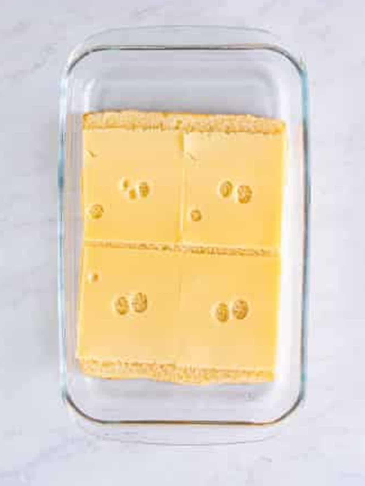 Swiss cheese slices layered on Hawaiian roll bottoms in a baking dish.