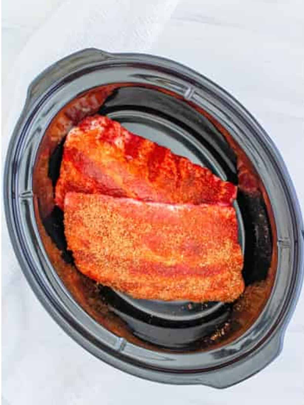 Seasoned baby back ribs placed in the slow cooker.