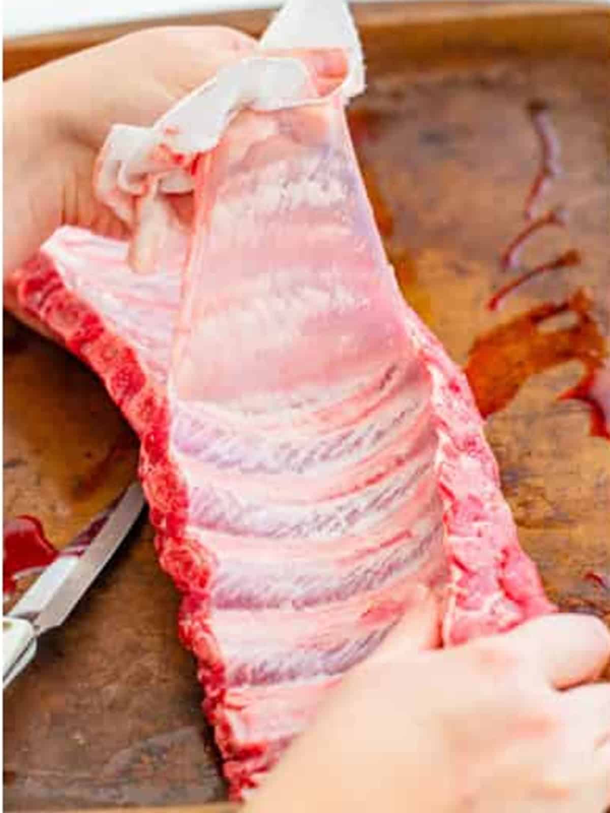 Removing the back membrane from a rack of baby back ribs.