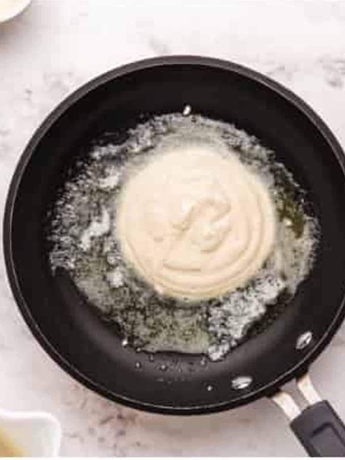 A ricotta pancake cooking in butter in a skillet.