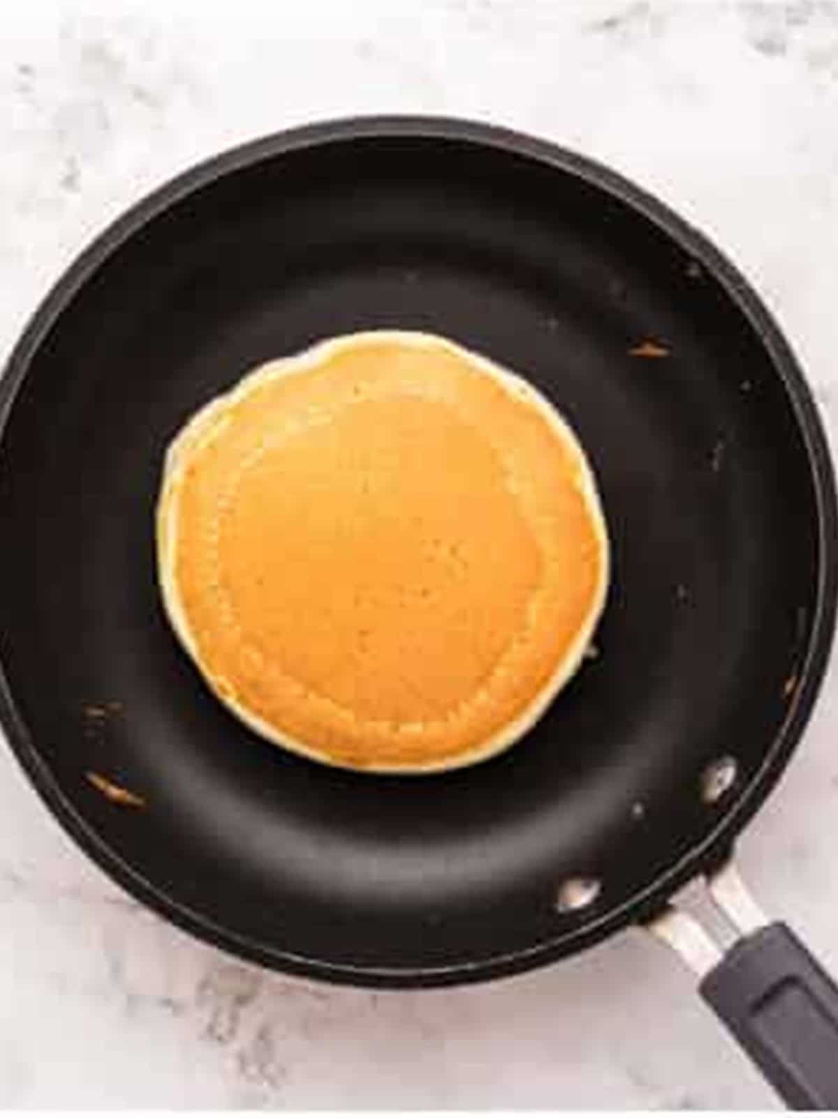 A golden brown ricotta pancake flipped in the skillet.