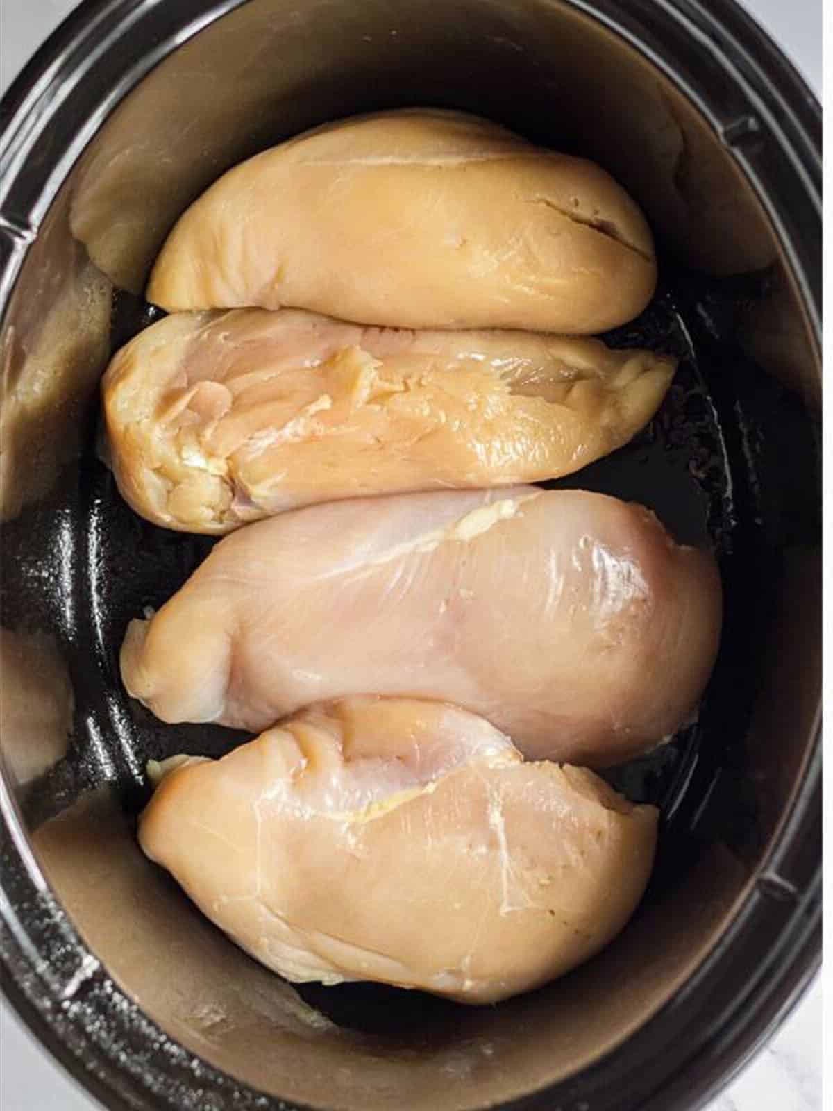 Boneless chicken breasts placed in a slow cooker.