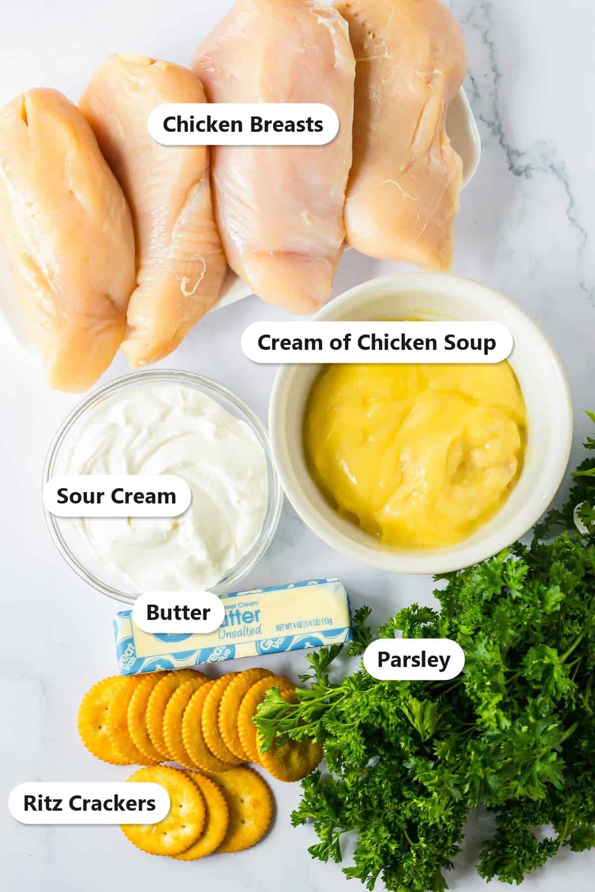 Labeled ingredients for slow cooker Ritz cracker chicken including chicken breasts, cream of chicken soup, sour cream, butter, Ritz crackers, and parsley.