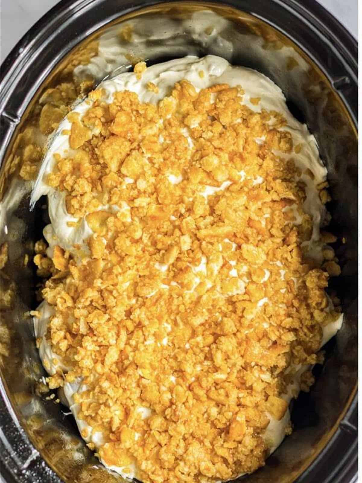 Creamy sauce and buttery Ritz cracker crumbs spread over chicken in a slow cooker.