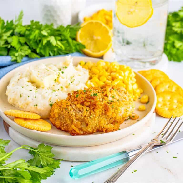 Two golden Ritz cracker baked pork chops on a plate with lemon wedges and fresh parsley.