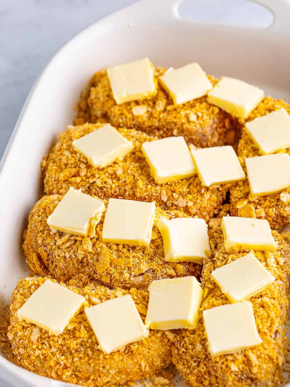 Breaded Ritz cracker pork chops arranged in a white baking dish topped with cubes of butter.