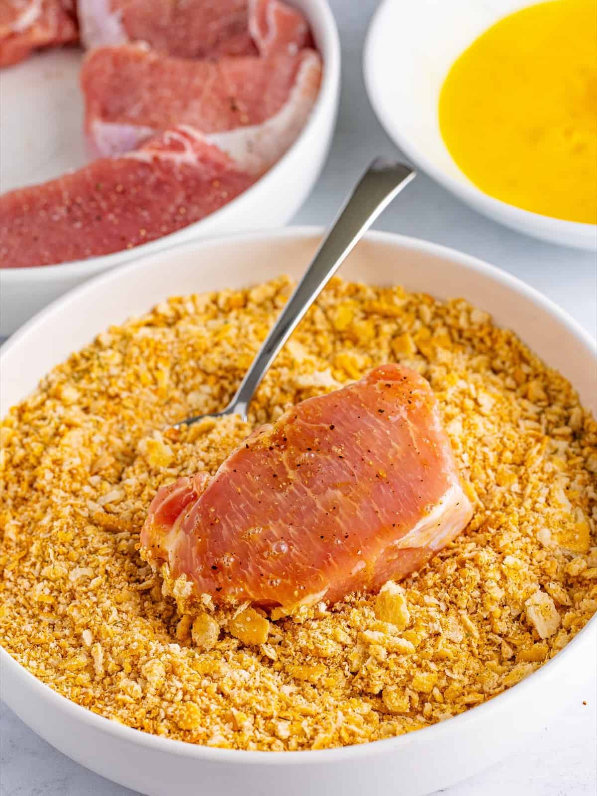 A pork chop pressed into seasoned Ritz cracker crumbs to fully coat both sides.