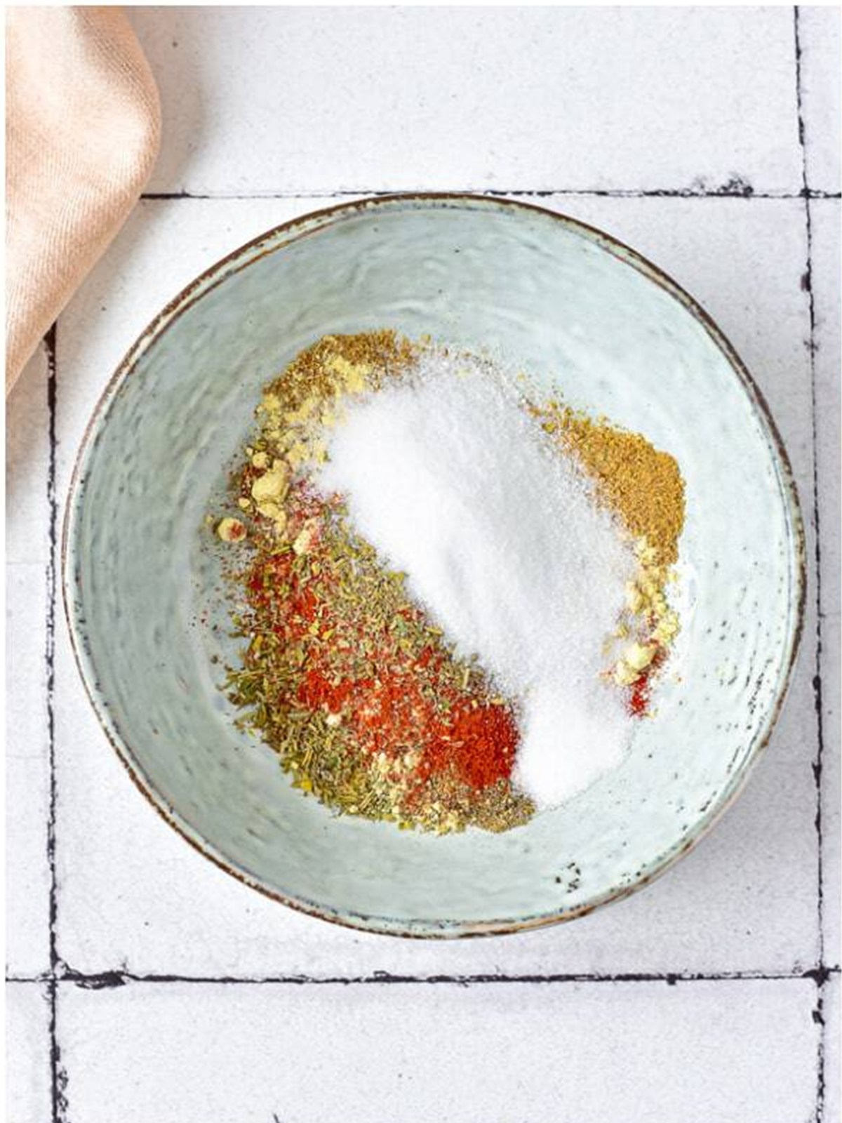 Salt, pepper, Italian seasoning, and paprika mixed in a bowl for roast chicken.