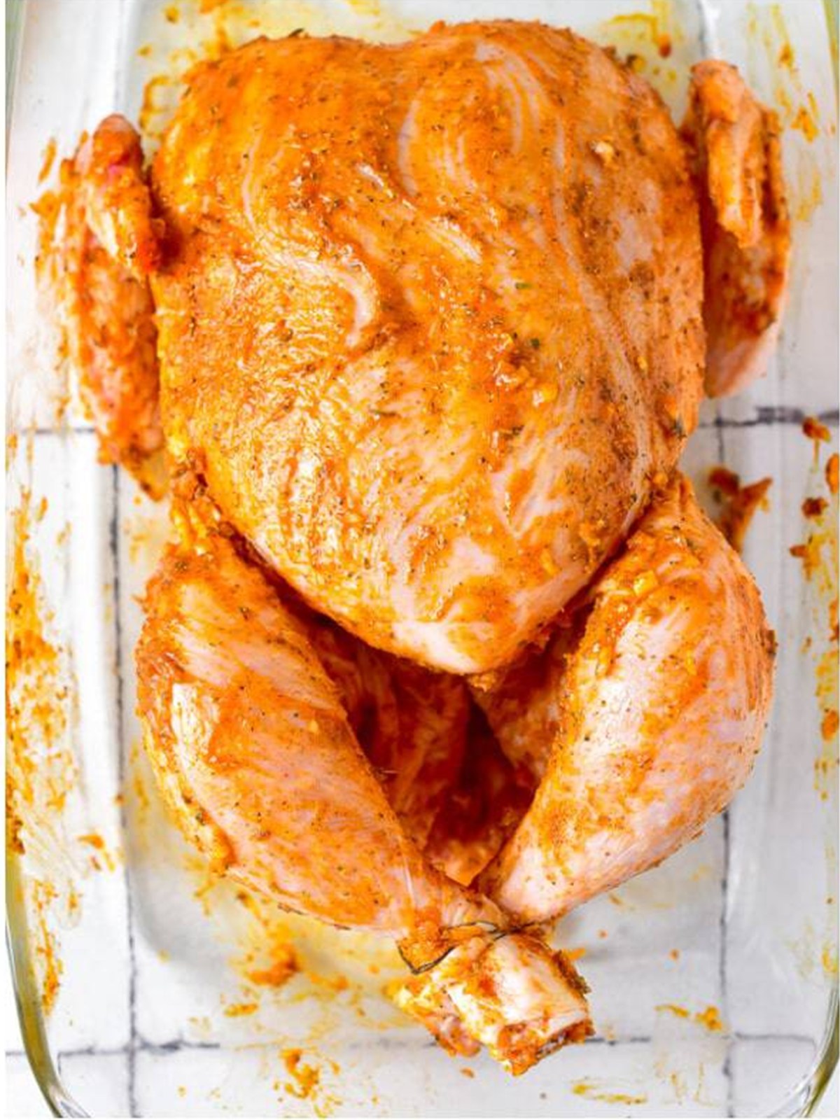 Raw whole chicken rubbed all over with the garlic butter herb paste in a baking dish.