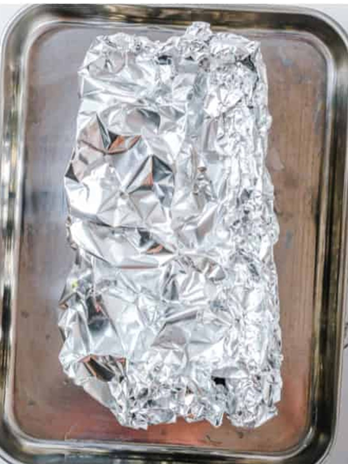 A foil-wrapped packet of garlic sitting in a metal baking dish ready to roast.