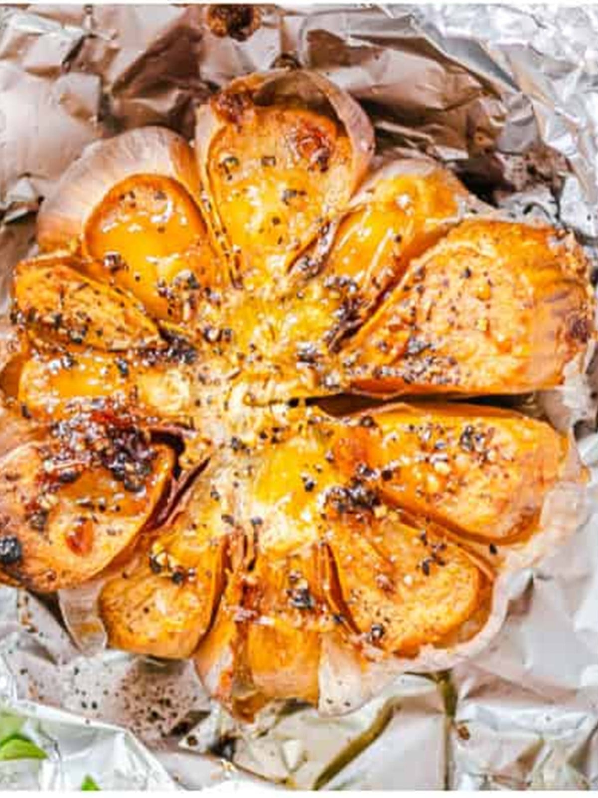 A head of roasted garlic with soft, golden, caramelized cloves in opened foil.