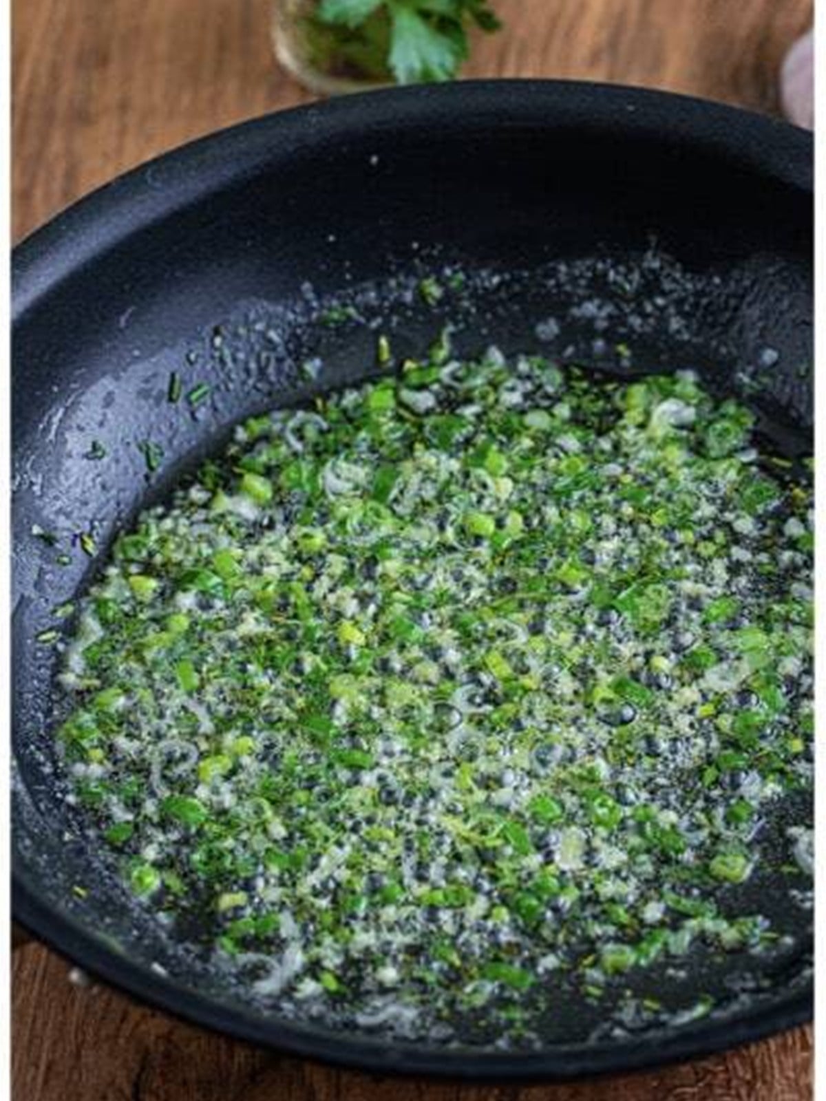 Butter, scallion, and herbs cooking in a skillet.