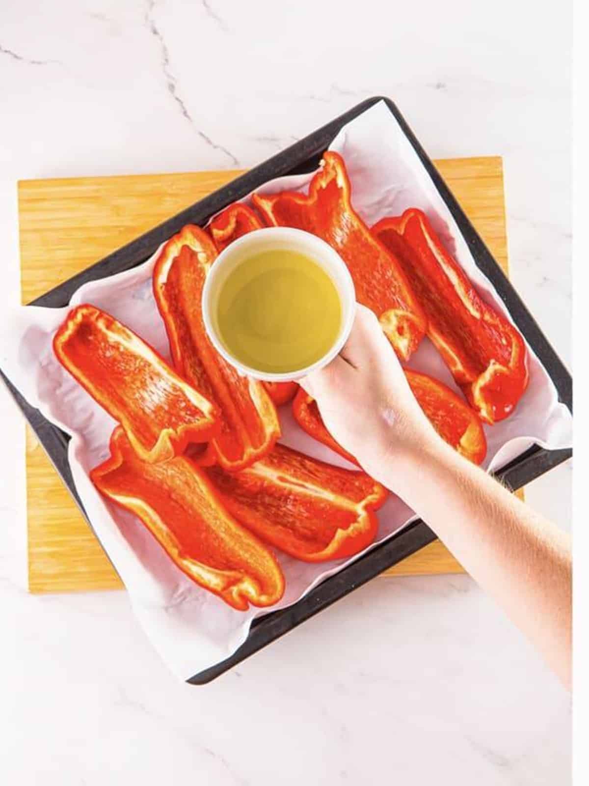 Quartered red bell peppers on a sheet tray being drizzled with olive oil.