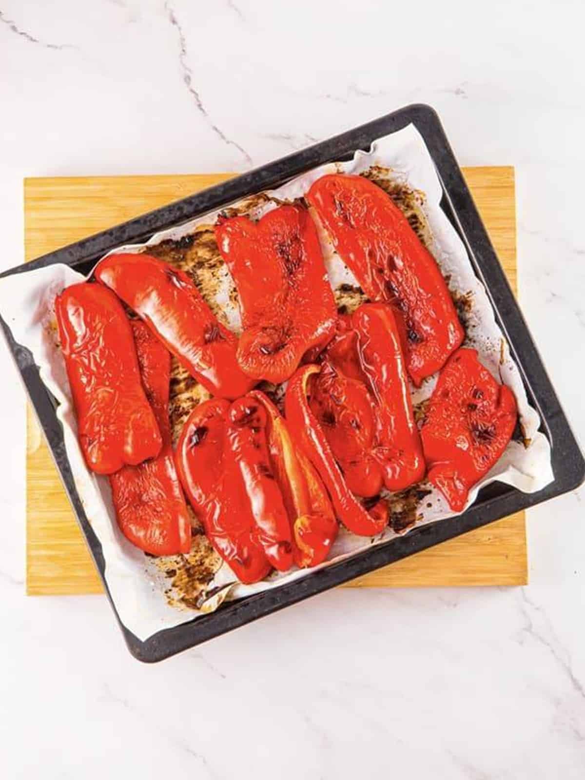 Charred roasted red bell peppers fresh from the oven on a sheet tray.