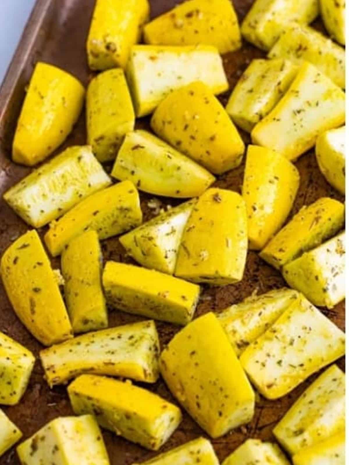 Seasoned yellow squash arranged in a single layer on a sheet tray.