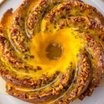A glazed bundt rum cake topped with pecans on a serving plate.