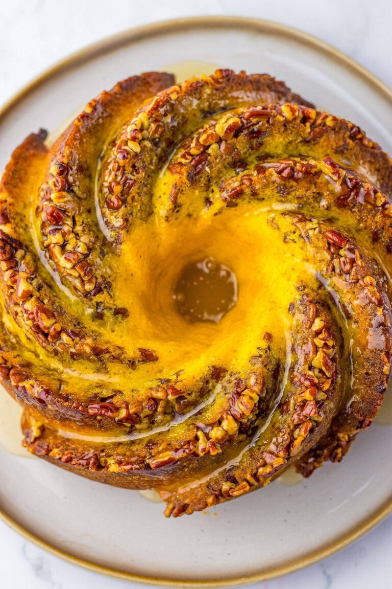 A glazed bundt rum cake topped with pecans on a serving plate.