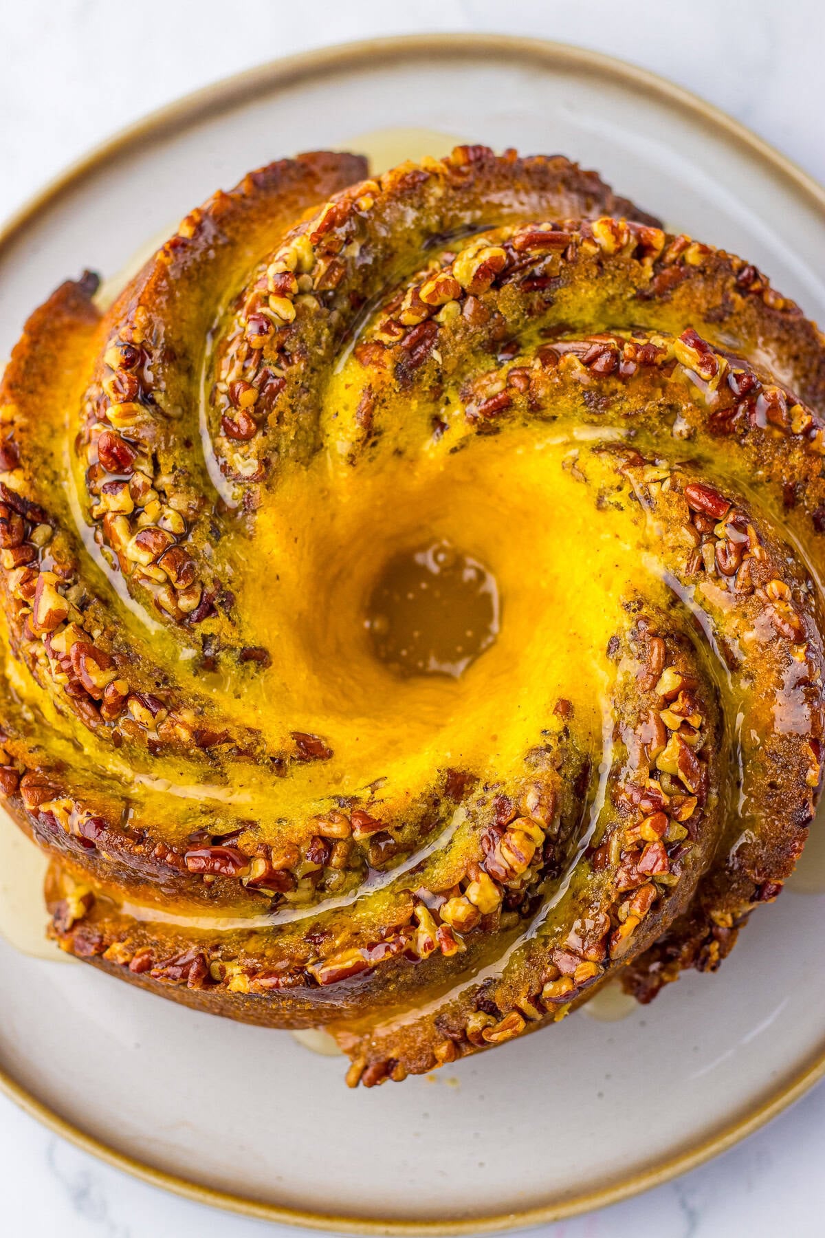 A glazed bundt rum cake topped with pecans on a serving plate.