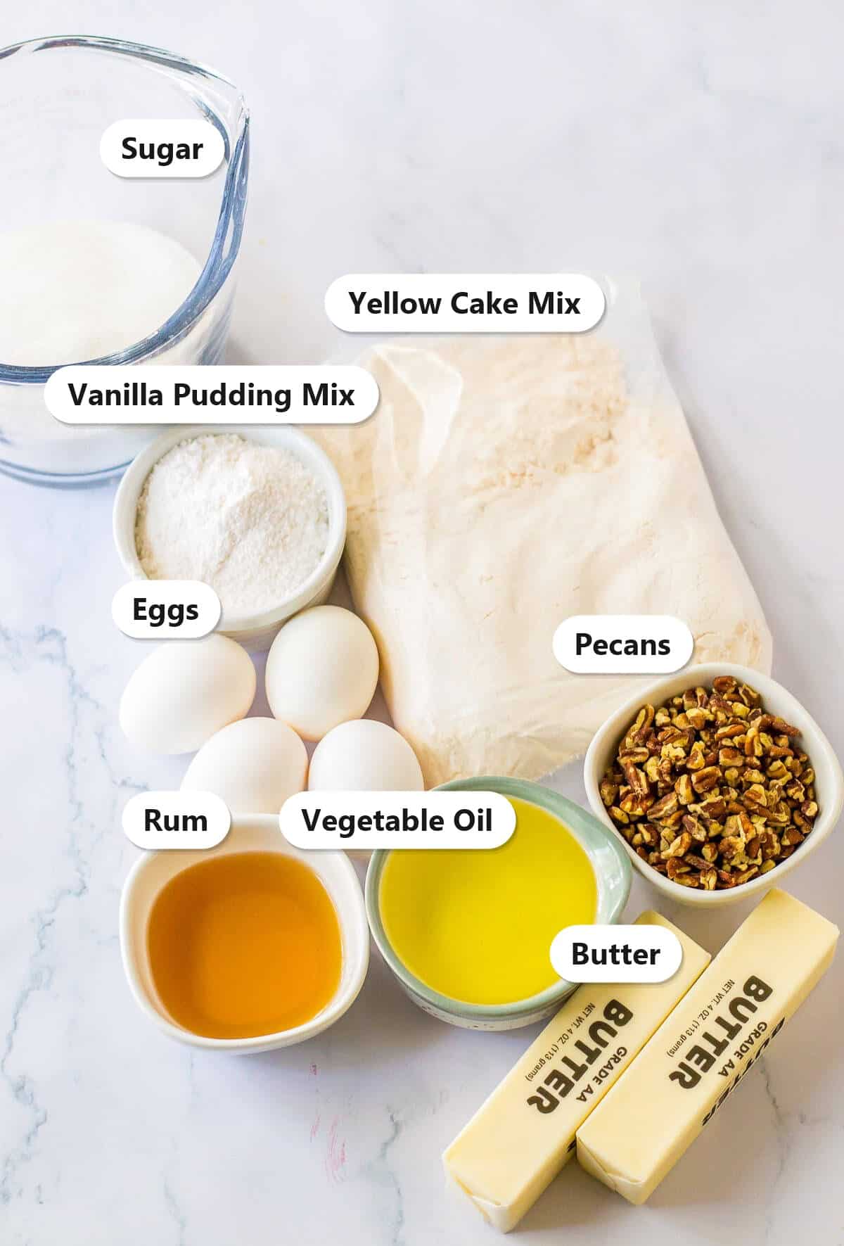 Labeled ingredients for rum cake including yellow cake mix, vanilla pudding mix, eggs, sugar, rum, vegetable oil, pecans, and butter.