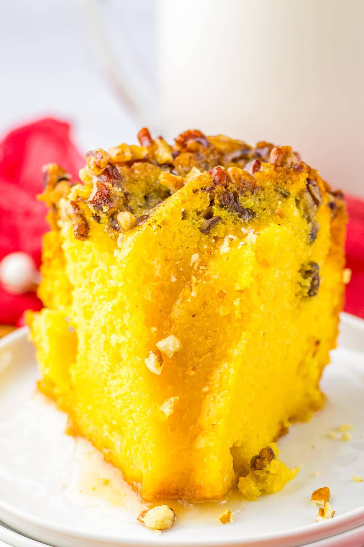 A slice of moist rum cake with pecans on a white plate.
