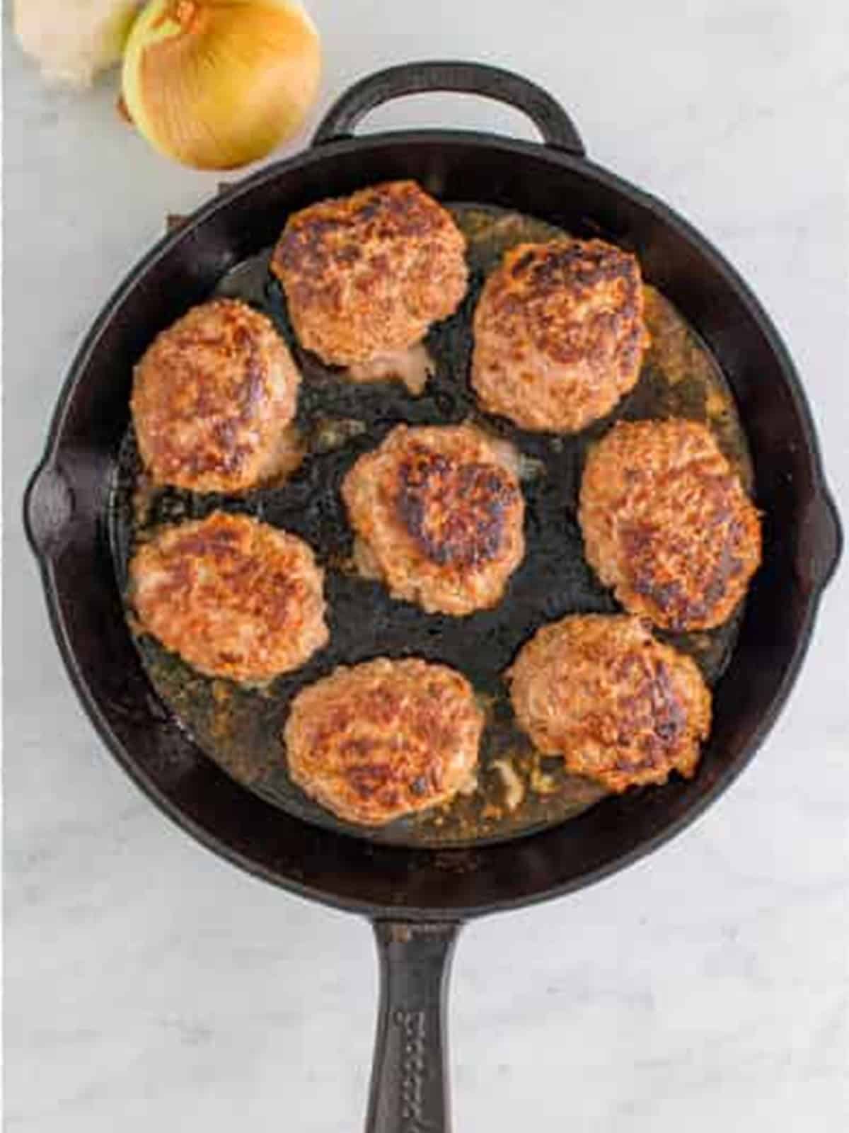 Salisbury steak patties browning in a cast iron skillet.