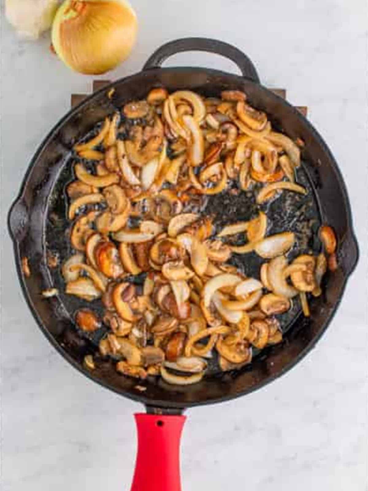 Sliced onions and mushrooms cooking in butter in a skillet.
