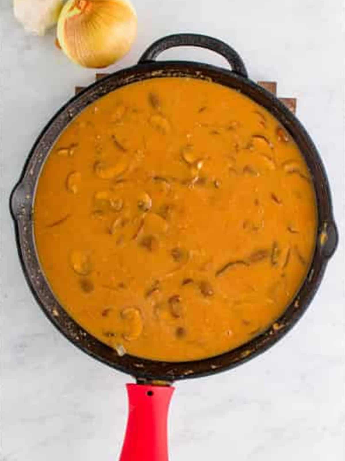 Whisking beef stock into the flour and mushrooms to make brown gravy.