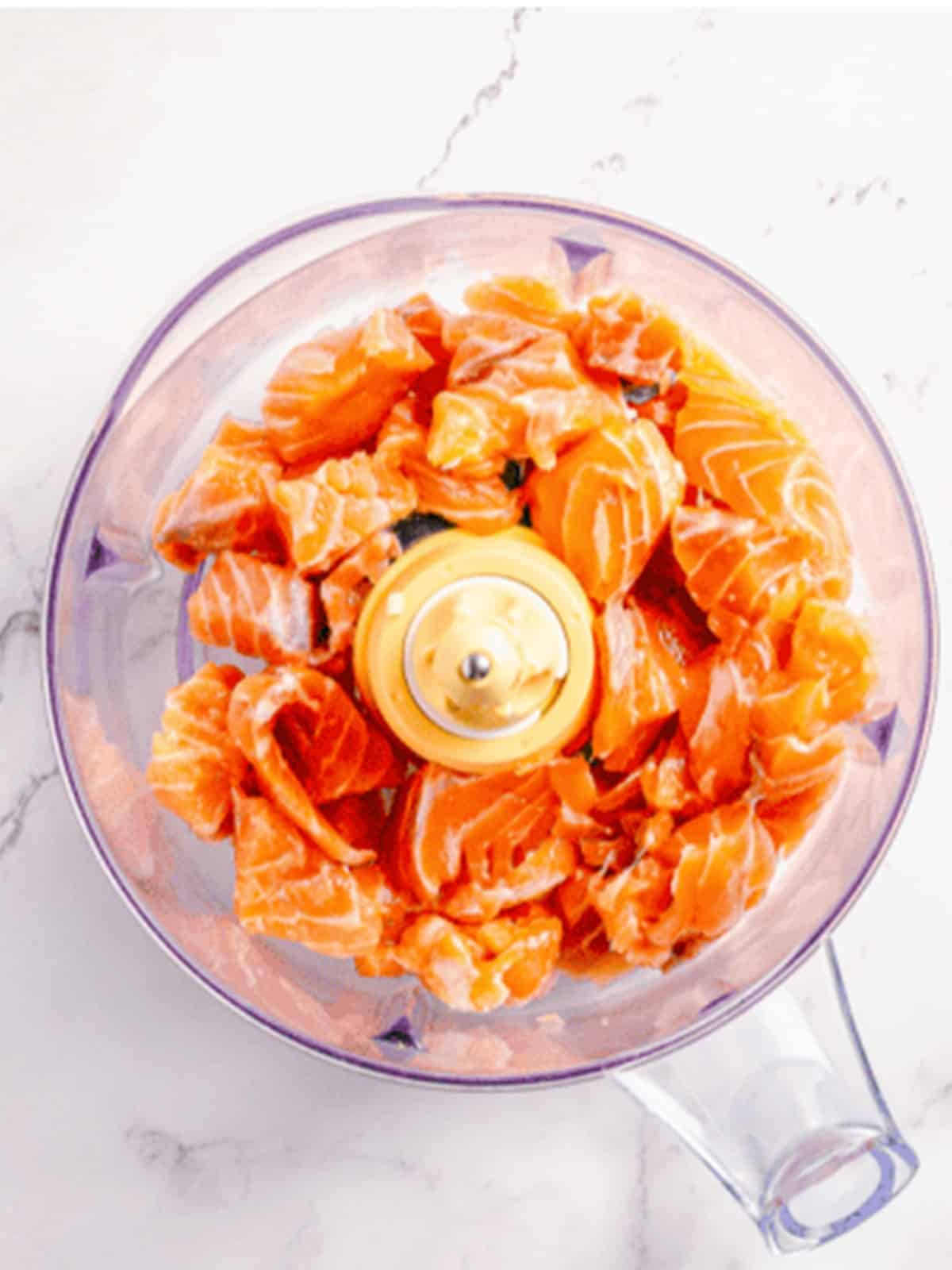 Fresh salmon chunks in a food processor to make salmon burger patties.