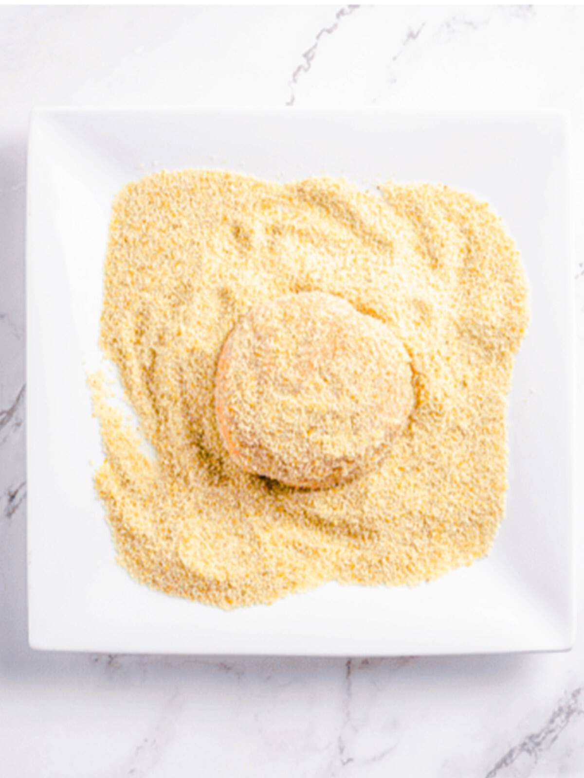 Coating a salmon patty in breadcrumbs before frying.