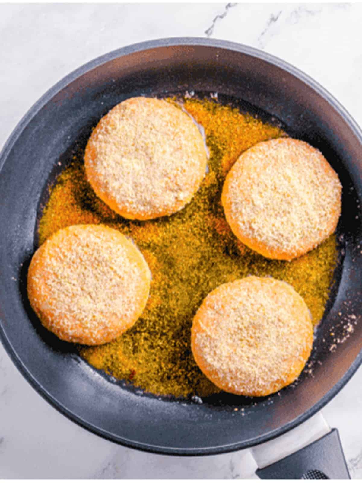 Frying breaded salmon burger patties in oil until golden brown.
