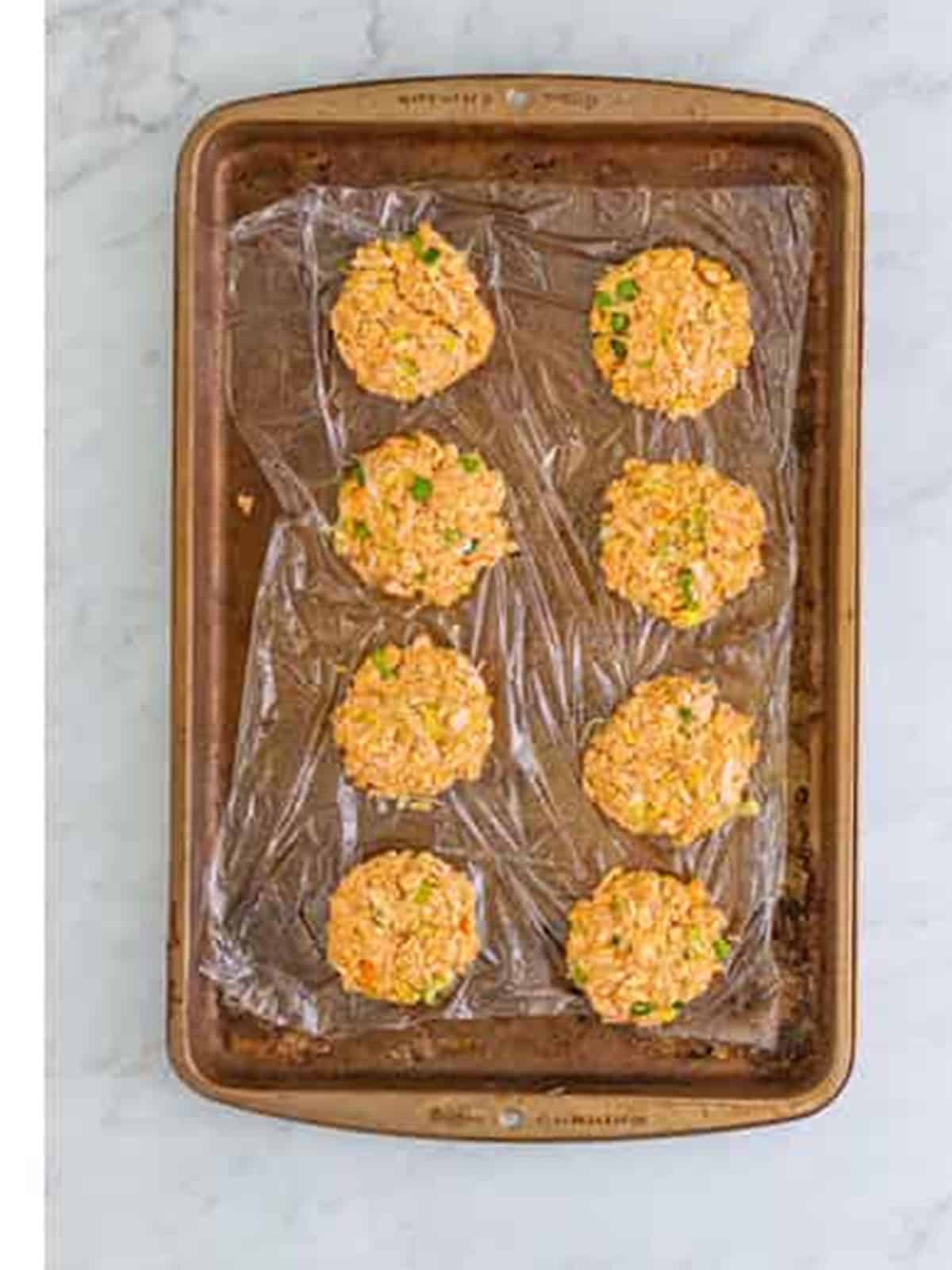 Eight formed salmon patties on a plastic lined sheet tray before chilling.