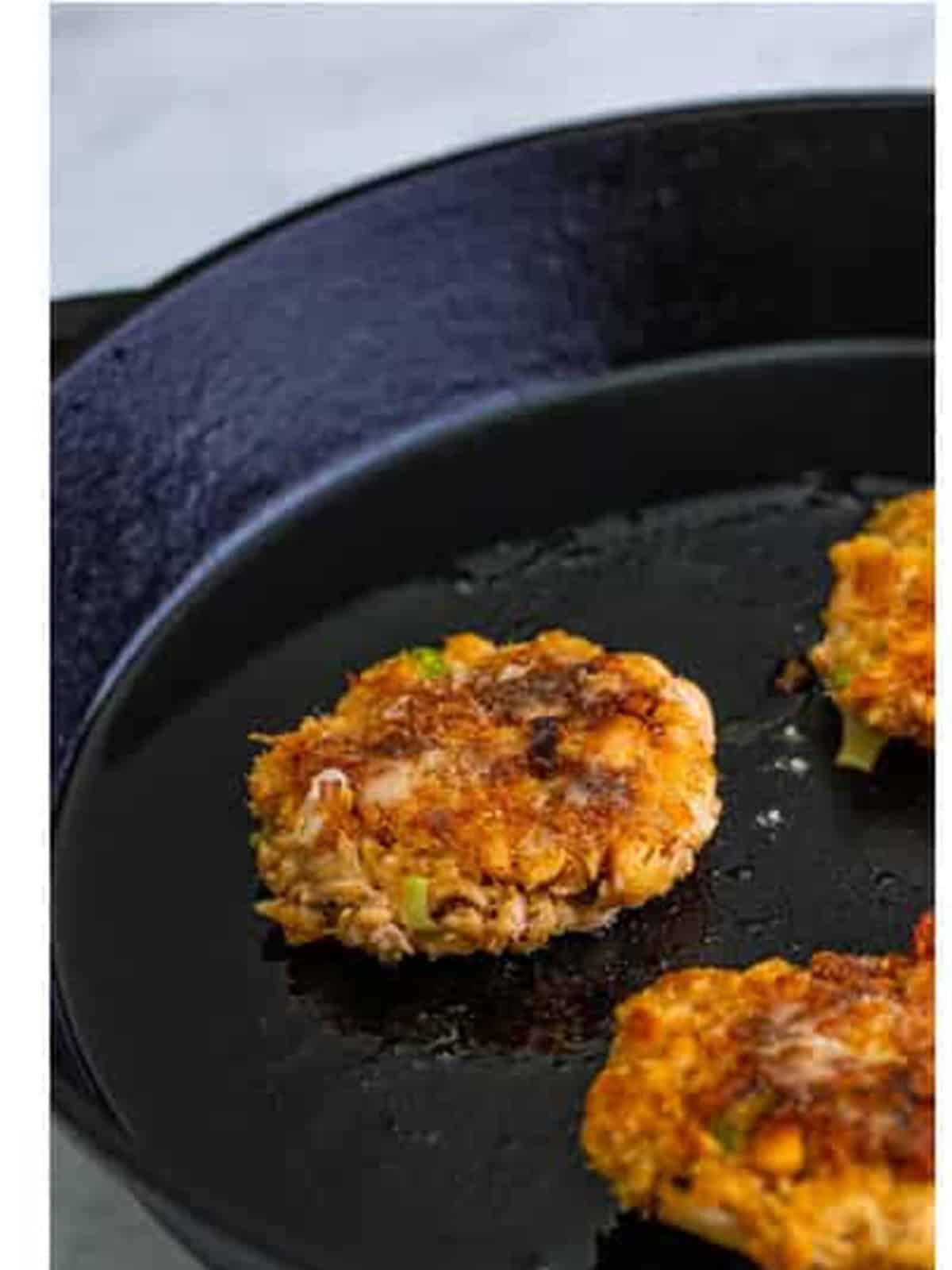 Salmon patties pan frying in a cast iron skillet until golden brown.