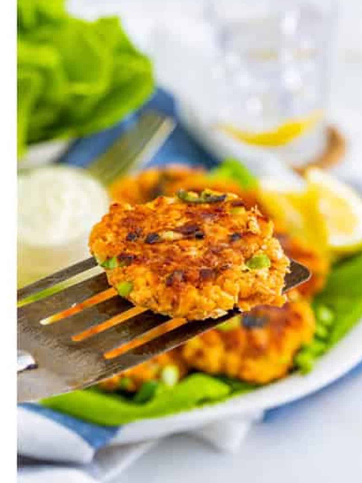Golden brown salmon patty served on a spatula with lettuce and lemon wedges.